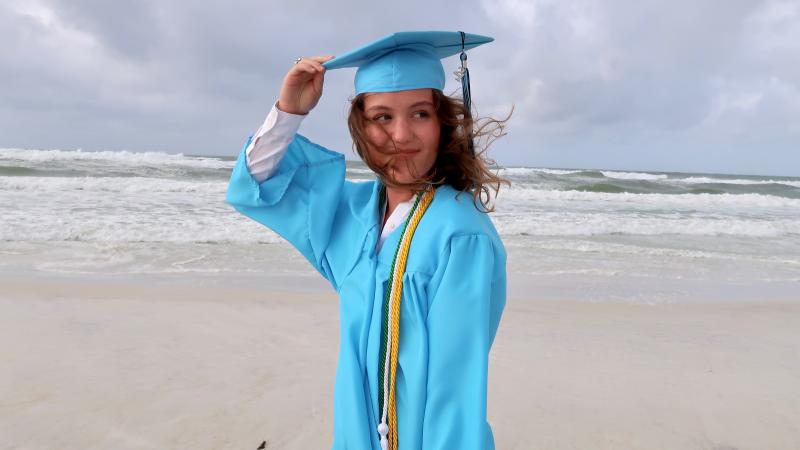 A girl on the beach wearing a graduation cap and gown